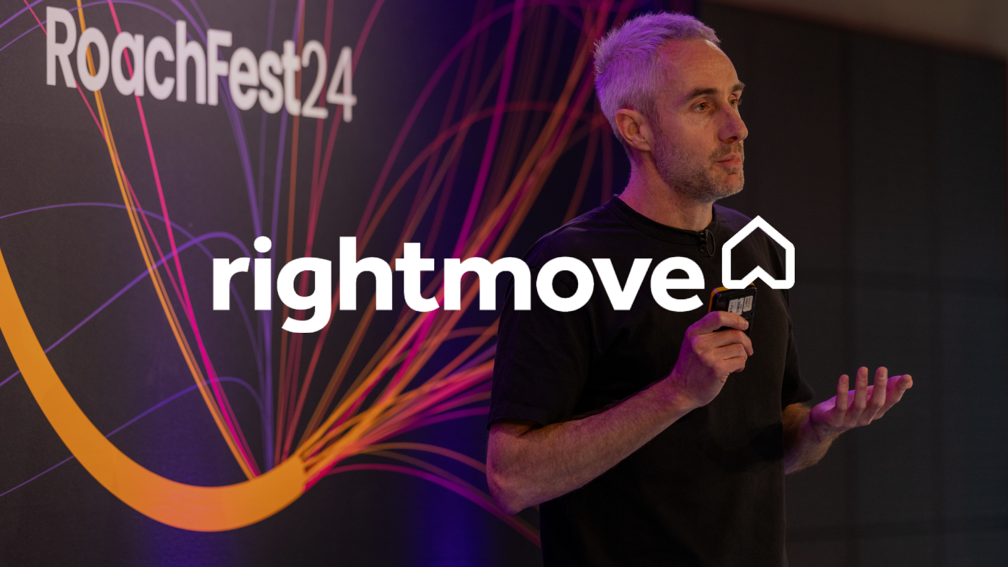 Andrew Tate, Rightmove's Head of Technology Operations, stands on the RoachFest24 London stage, giving a presentation. The Rightmove logo is superimposed on the image.